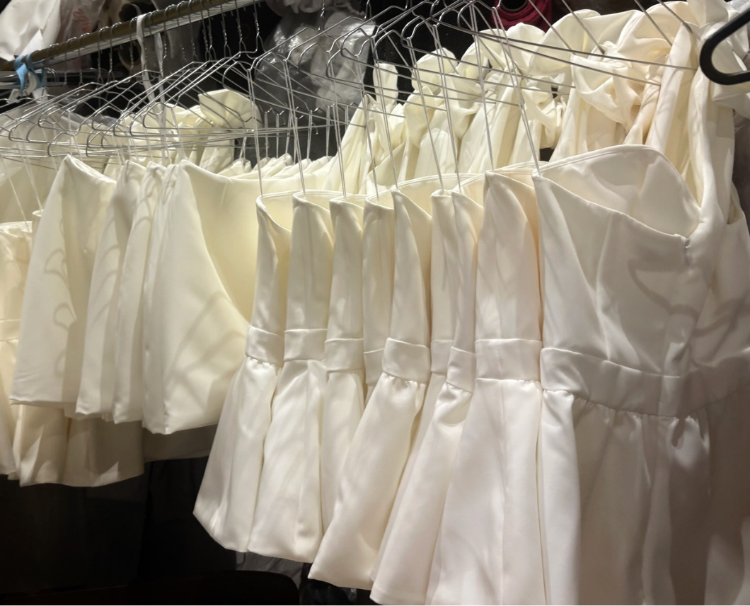 Row of white tops and skirts on hangers in a sewing room setting