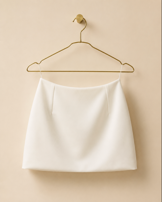 Back View of white mini skirt on a gold hanger against a beige background